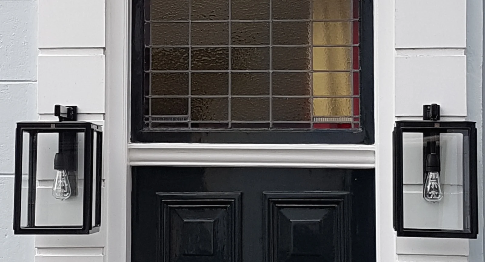 Twee Amsterdam-wandlampen aan weerszijden van de voordeur.
