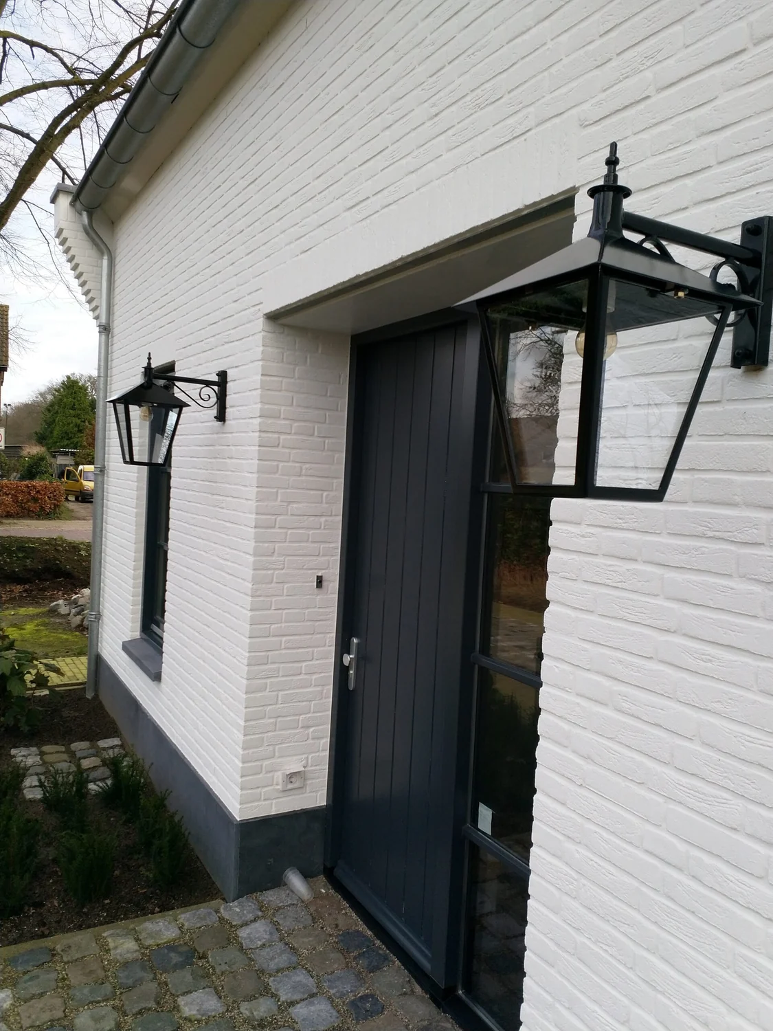 Een lantaarn op een hangende muurarm aan een witte gevel.