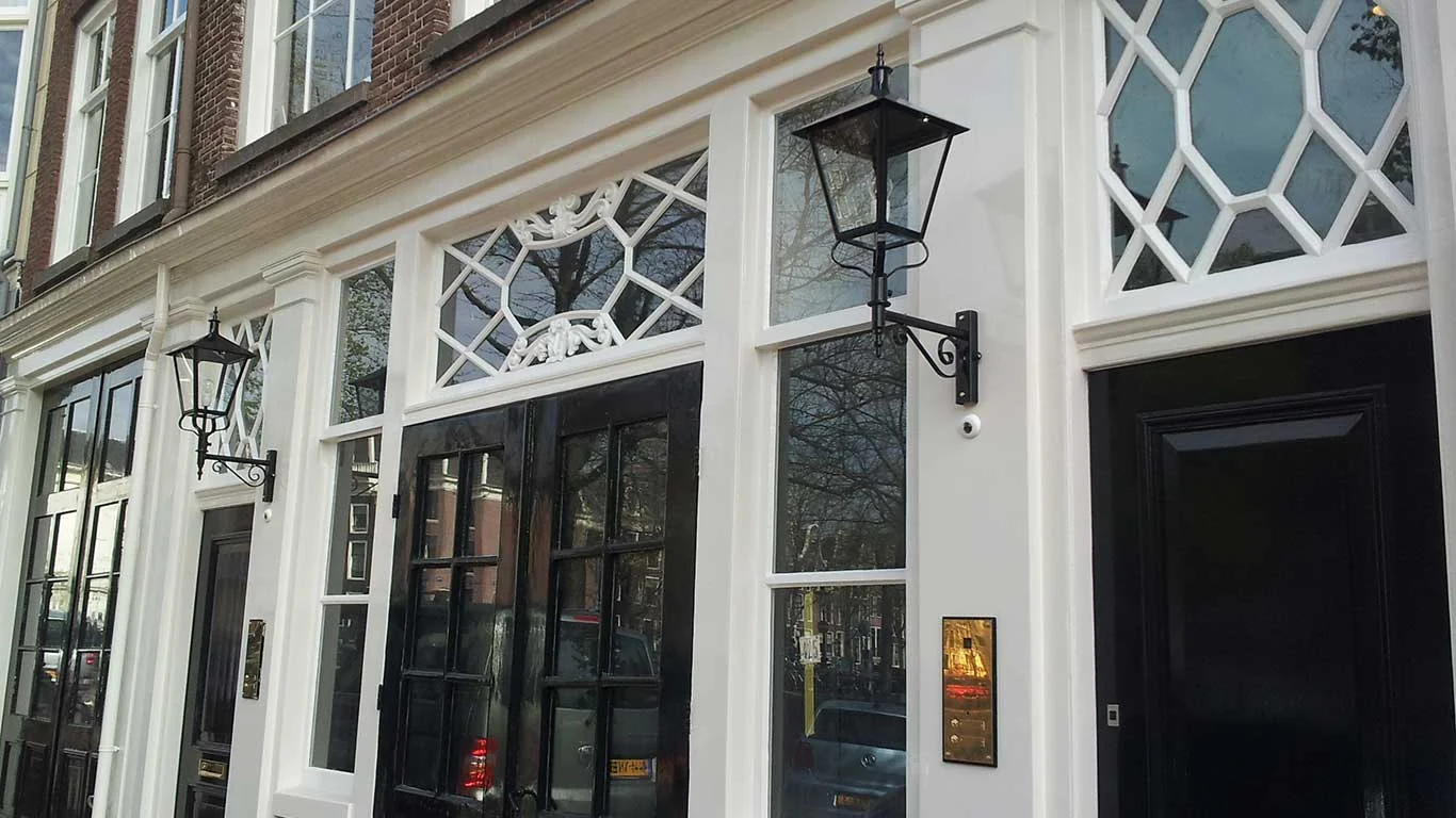 Lantaarns op staande muurarmen bij een gevel met hoge ramen.