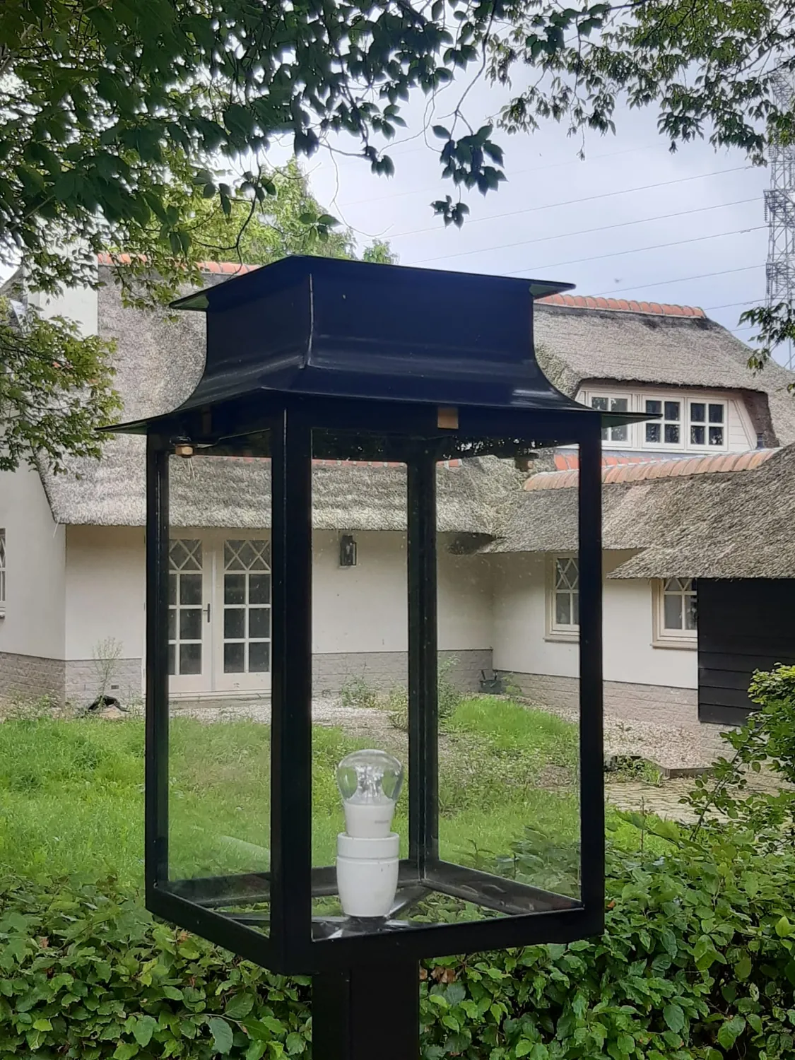 Een lantaarn tussen het groen, met de woning op de achtergrond.