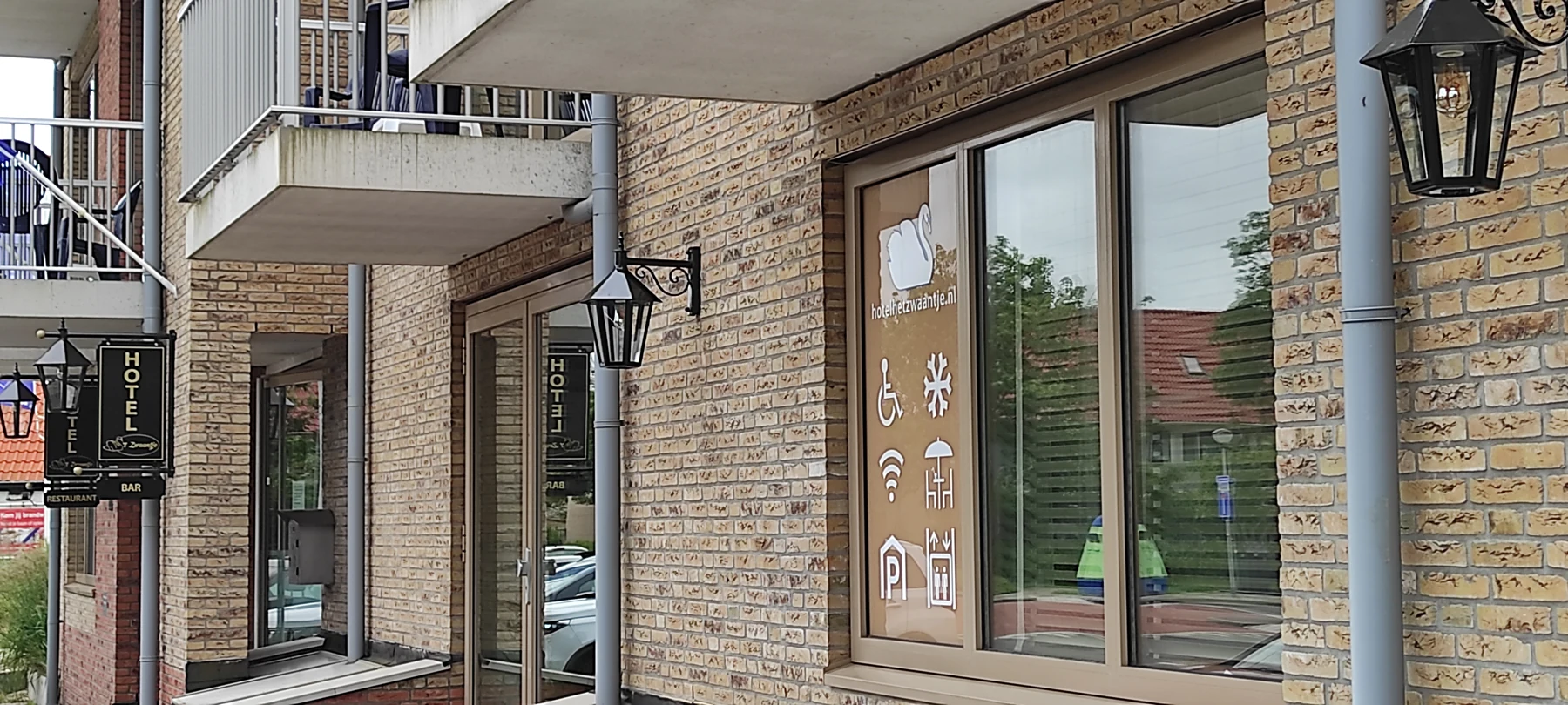 Artisans Zeskant L-lantaarns op hangende muurarmen langs Hotel Het Zwaantje, met een bijzondere uitvoering rond het uithangbord.