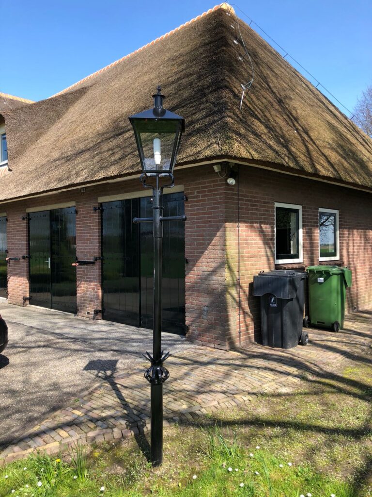 Zwarte lantaarnpaal naast een bakstenen woning met een rieten dak.