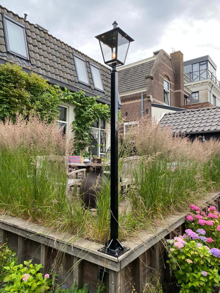 Zwarte lantaarnpaal tussen hoge siergrassen bij een terras.